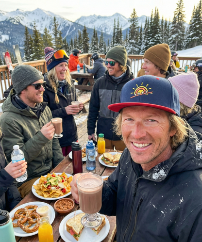 Group of people enjoying a meal and drinks outdoors with a snowy mountain background